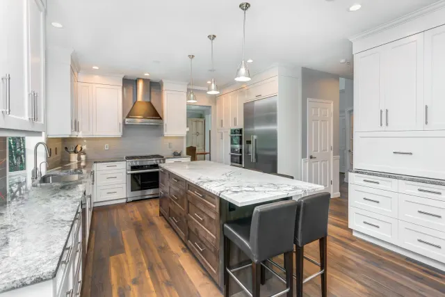 White kitchen with a marble-topped island and dark hardwood flooring.